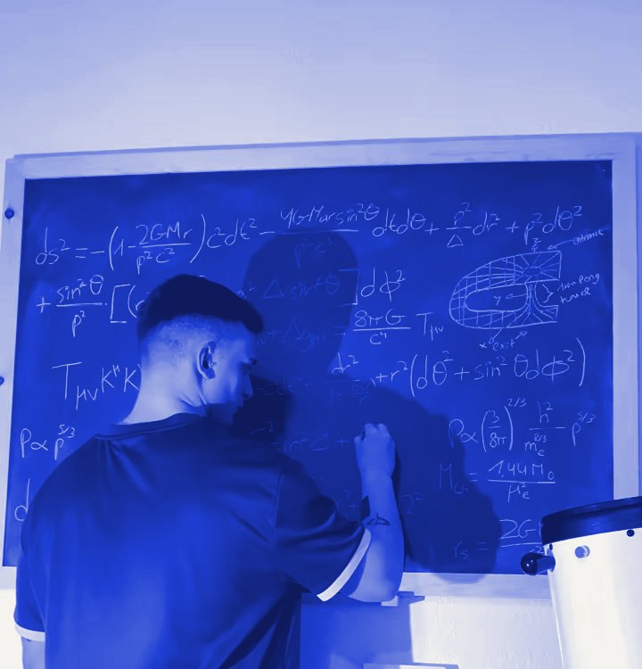 Lluc Sánchez, de espaldas, escribiendo ecuaciones de relatividad en una pizarra, junto a un telescopio